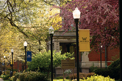 A tree-lined street with light poles and Wilkes University flags on the Wilkes University campus in Wilkes-Barre, PA.
