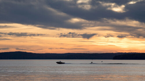 A speed boat pulls a water skier across a calm Lake Wallenpaupack in Hawley, PA, at sunset, a top destination in the Pocono Lake Region.