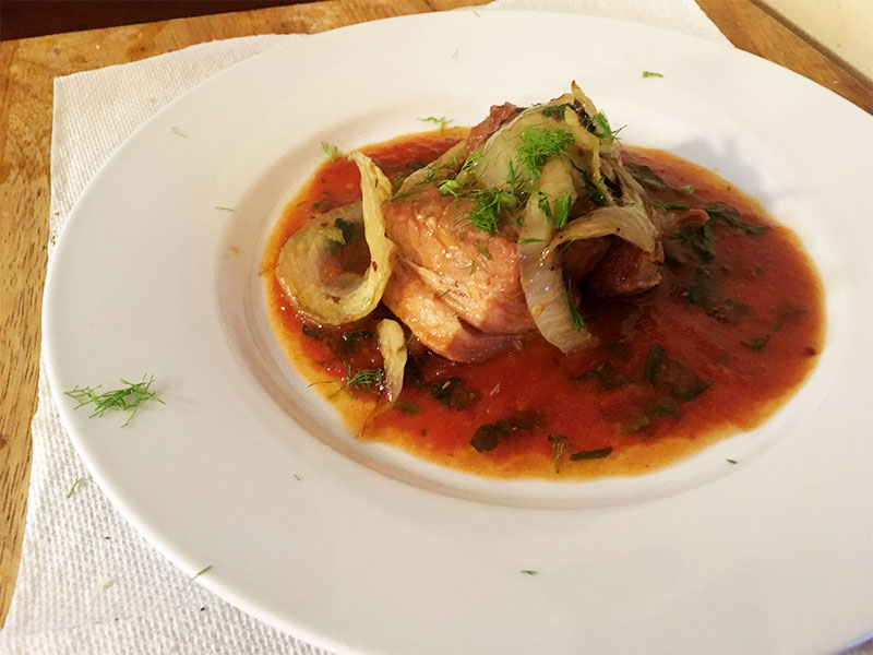 A plated dish featuring a protein in a rich red sauce, garnished with caramelized onions and fresh dill from Old Tioga Farm in Stillwater, PA.
