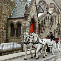 Two white horses pull a carriage with a driver in a top hat on a street in Jim Thorpe, Pennsylvania, during the Winterfest celebration.