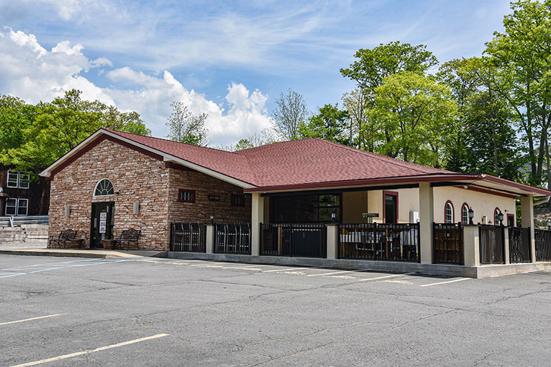 The exterior of Three Guys Restaurant and Sports Bar in Mountain Top, PA. It's a light brick building with a red awning and patio area.