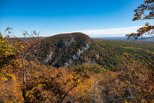 A landscape view of Mount Minsi within the Delaware Water Gap National Recreation Area during autumn, showcasing fall foliage and a clear blue sky.