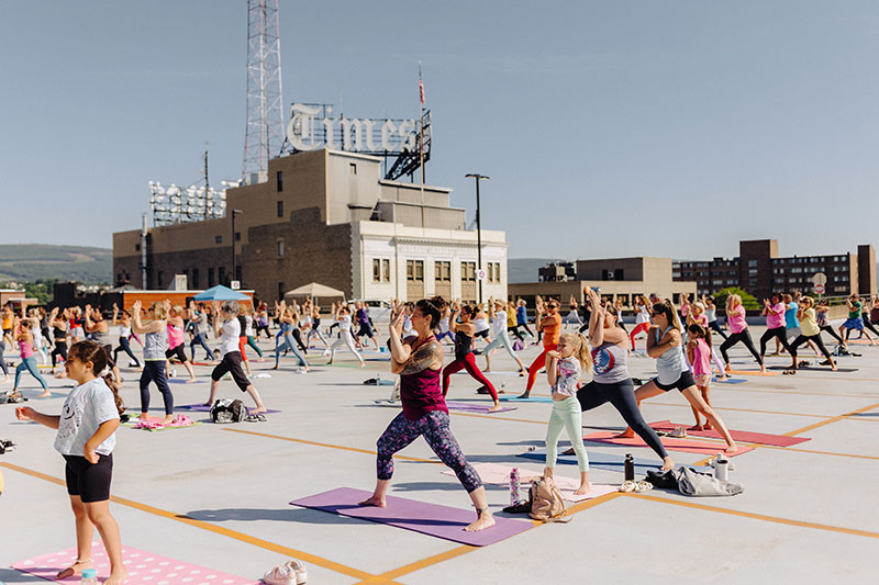 A large group of yoga students participating in a Jaya Yoga class on a rooftop overlooking the Scranton Times Building in Scranton, PA.