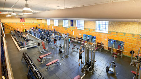 The Wilkes-Barre Family YMCA offers a spacious gym with a variety of exercise equipment, including treadmills, stationary bikes, weight machines and free weights. People are working out on the machines and using the free weights.
