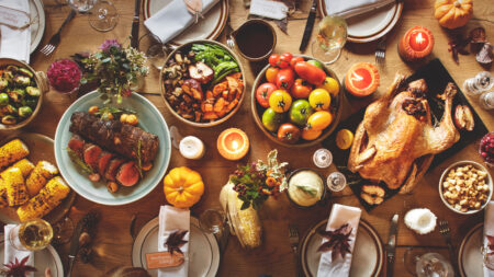 An overhead view of a Thanksgiving dinner table, set with a roasted turkey, bowls of colorful vegetables, sides, and place settings.