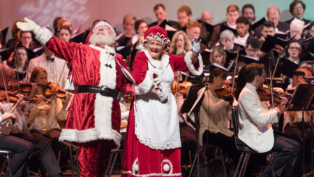 Santa and Mrs. Claus wave to the audience on stage with the NEPA Philharmonic Orchestra behind them.