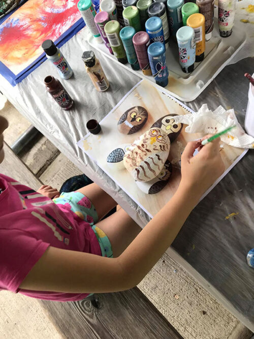 An overhead shot of a child sitting at a craft table painting a stone owl at Abington Art Studio in Clarks Summit, PA.
