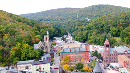 An aerial view of Jim Thorpe, Pennsylvania, nestled in a valley with St. Mark's Episcopal Church and other buildings visible among the fall foliage.