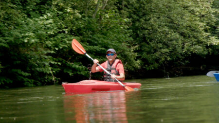 A man in a red kayak paddles down the Lackawanna River in the summertime.