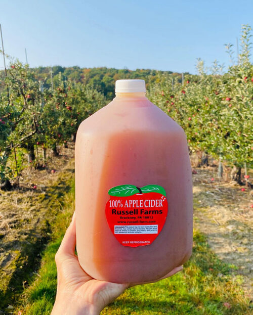 Gallon of cider held up in front of the apple orchard at Russell Farms in Brackney, PA.