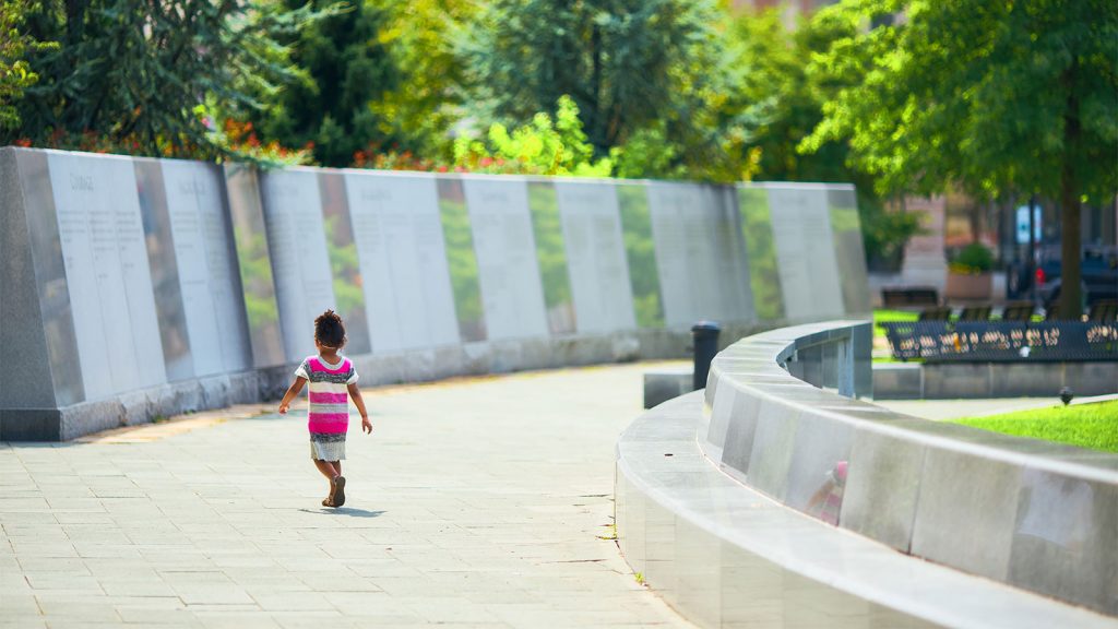 A young girl walks along a paved pathway in front of a memorial wall at Courthouse Square in downtown Scranton, PA.