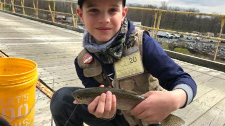 A young man decked out in fishing gear shows off a nice rainbow trout he caught from a fishing dock during Mentored Youth Trout Day.