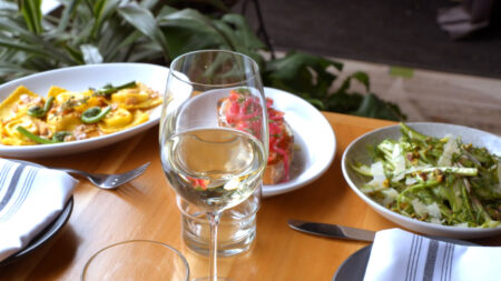 A table setting with a glass of white wine, a plate of ravioli, bruschetta, and a salad at Native in Honesdale, PA.