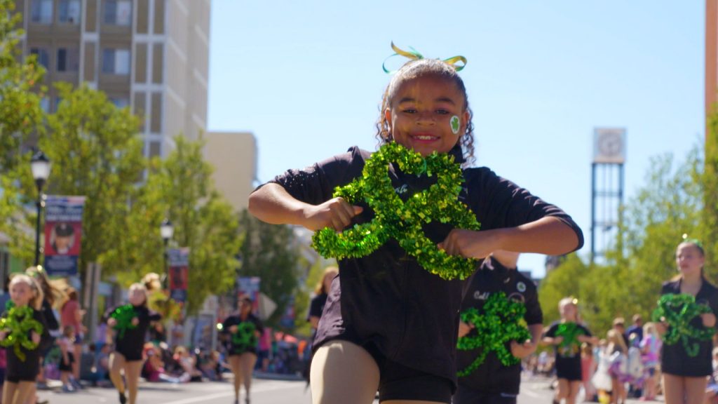 A young girl smiles and holds a green, glittery shamrock while participating in Wilkes-Barre's St. Patrick's Day parade with other children.