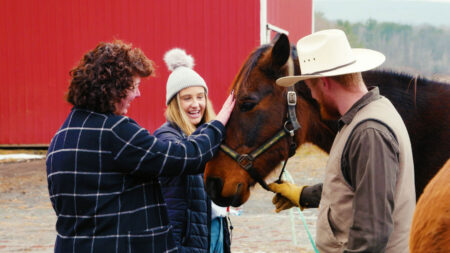 Two women and a horse trainer share a tender moment petting a friendly horse at Happy Trails Stables in Waymart, PA.