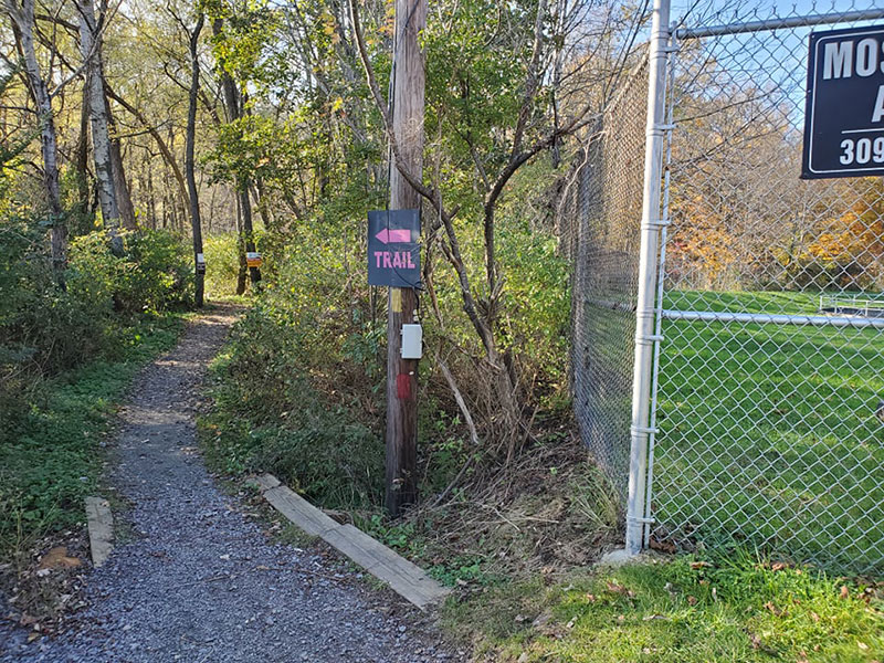 A small sign reading "Trail" is posted on a pole marking the trail's location next to a fence marking private property on the North Pocono Trail System in Moscow, PA.