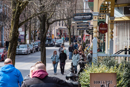 A street view of Jim Thorpe, PA with pedestrians walking and cars driving by. Storefront signs are visible.