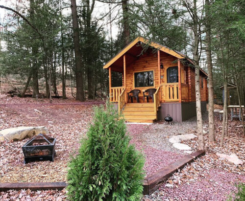 The exterior of a wood cabin with a fire pit outside at Lakewood Park Campground in Barnesville, PA.