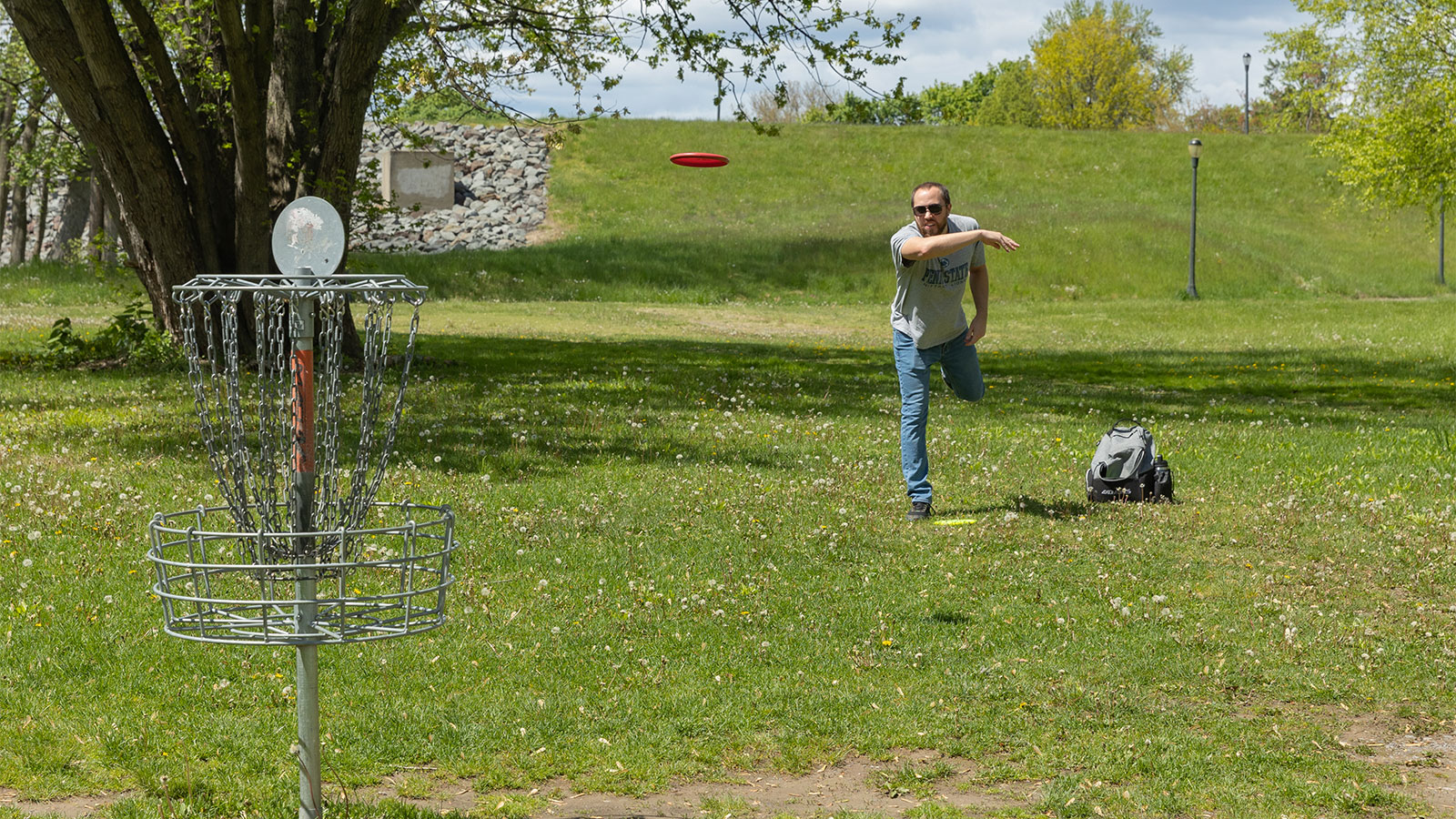 A man in a short sleeve shirt and jeans throwing a frisbee while playing disc golf at Nesbitt Park in Kingston, PA.