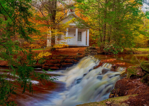 A stream and vibrant fall foliage leading up to a white chapel along a trail atHickory run State Park in White Haven, PA.