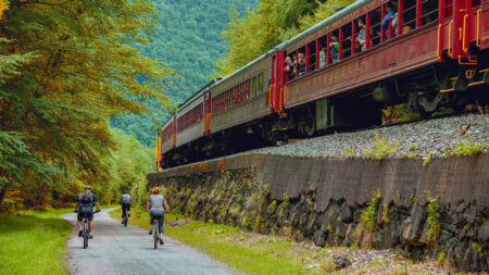 People biking next to the large red train on the tracks in Jim Thorpe, PA.