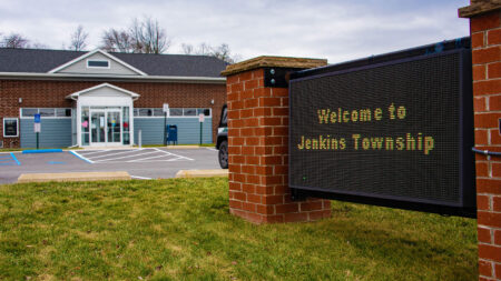 A digital sign between two brick columns in front of a building reads, 