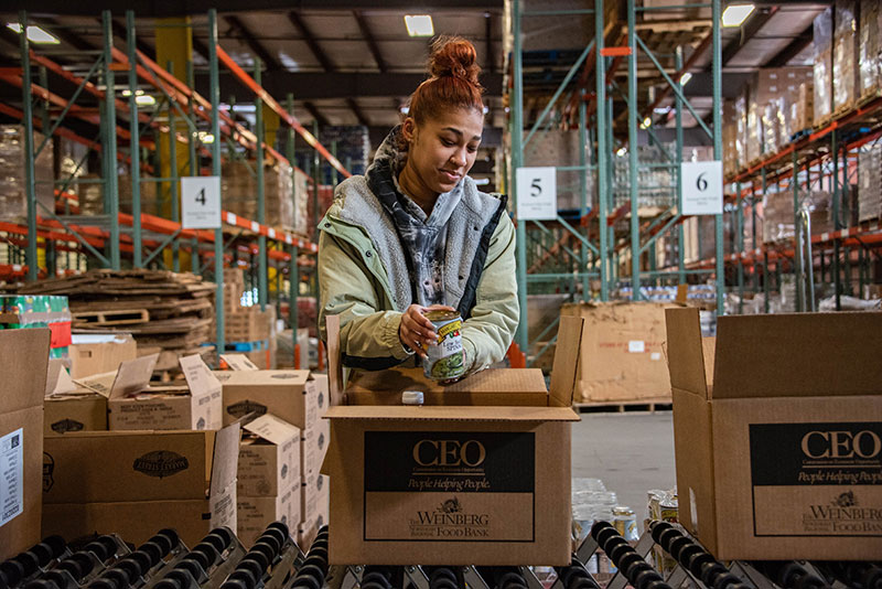 A female volunteer packs a box of food at the donation center. 