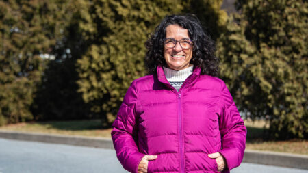 Gina Gargano stands in a pink jacket in front of pine trees outside her office at Explore Schuylkill in Pottsville, PA.