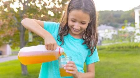 Girl in a teal shirt pouring a glass of NEEPA apple cider from a jug.