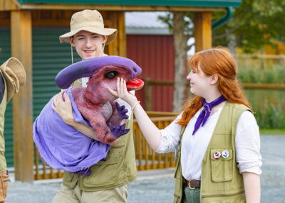 A young man in a safari hat holds a purple dinosaur puppet while a young woman with red hair gently touches its face during Jurassic Dino Fest at Roba Family Farms in North Abington Twp., PA.