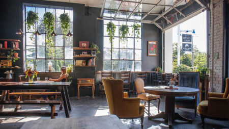 A wide view of the seating area at Cafe Wren with a large, open garage door and lots of hanging plants amidst the eclectic furniture in Milford, PA.