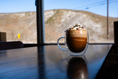 A glass mug of hot chocolate topped with whipped cream sits on a table at Perch at Jim Thorpe in Jim Thorpe, PA.