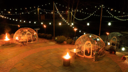 Three glowing dining igloos on a stone patio at night, surrounded by string lights and propane heaters at The Beaumont Inn in Dallas, PA.