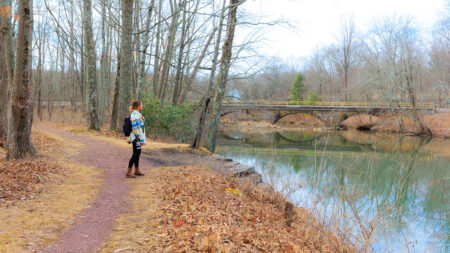 A woman stands on a hiking path while looking at the adjacent stream at the Landingville Marsh Trail in Schuylkill County, PA.
