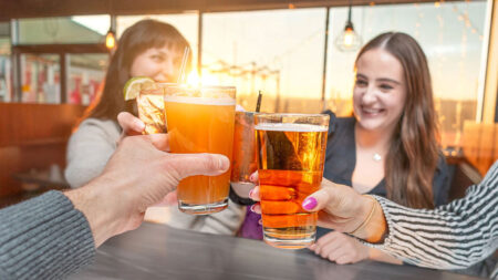 Cheers! Four friends clink beers and cocktails while sunset dining on the deck at River Grille in Wilkes-Barre, PA, a popular spot for happy hour deals in Northeastern PA.
