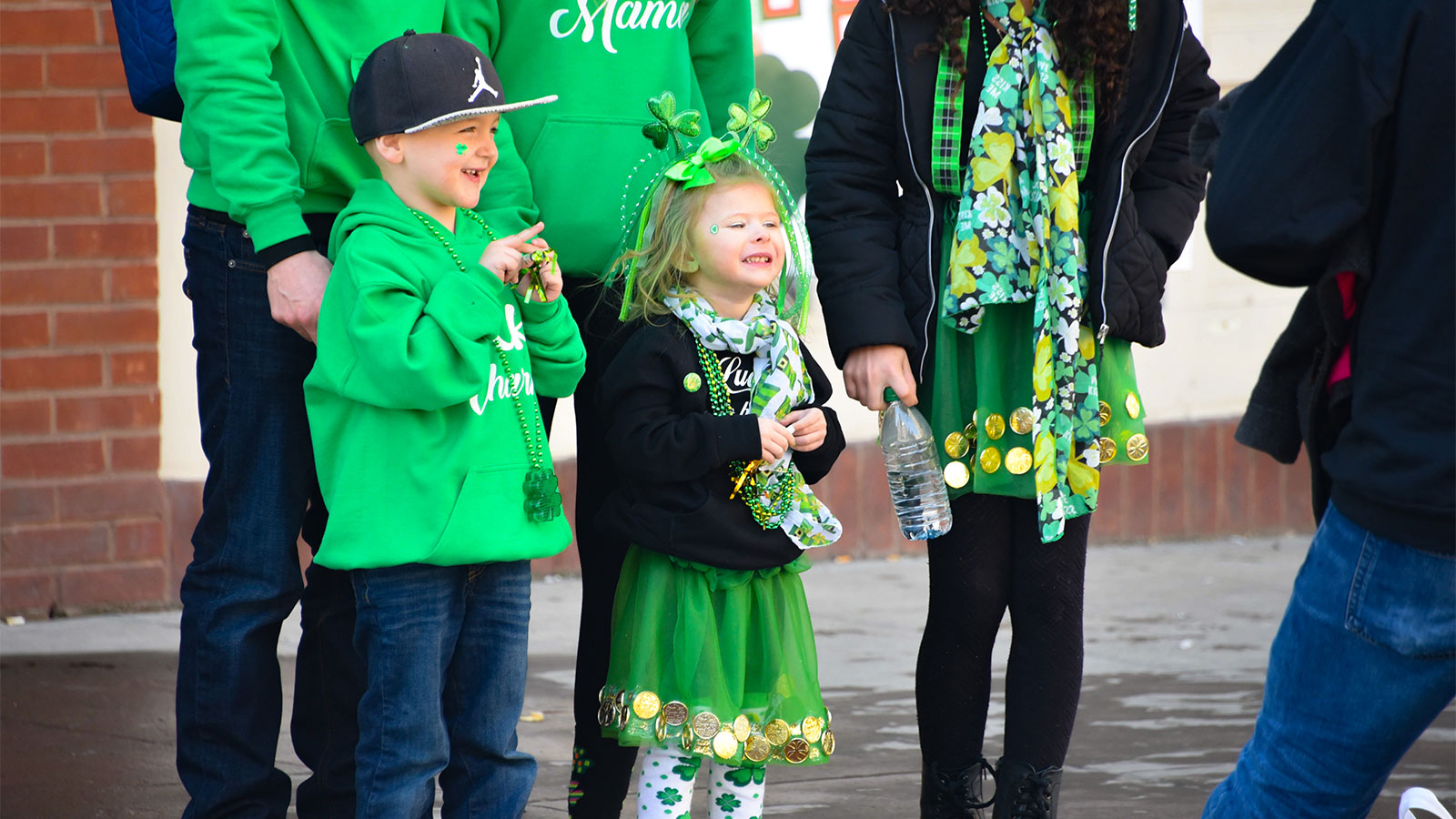 A group of people, including three children, dressed in green, with one child wearing a green tutu adorned with gold coins and shamrock-themed accessories during Scranton's St. Patrick's Day Parade.