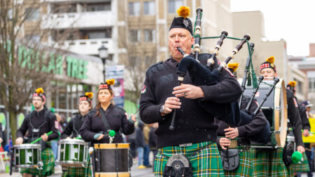 A group of musicians in traditional Scottish attire, including kilts and Glengarry bonnets, are performing in Wilkes-Barre's Annual St. Patrick's Day parade.