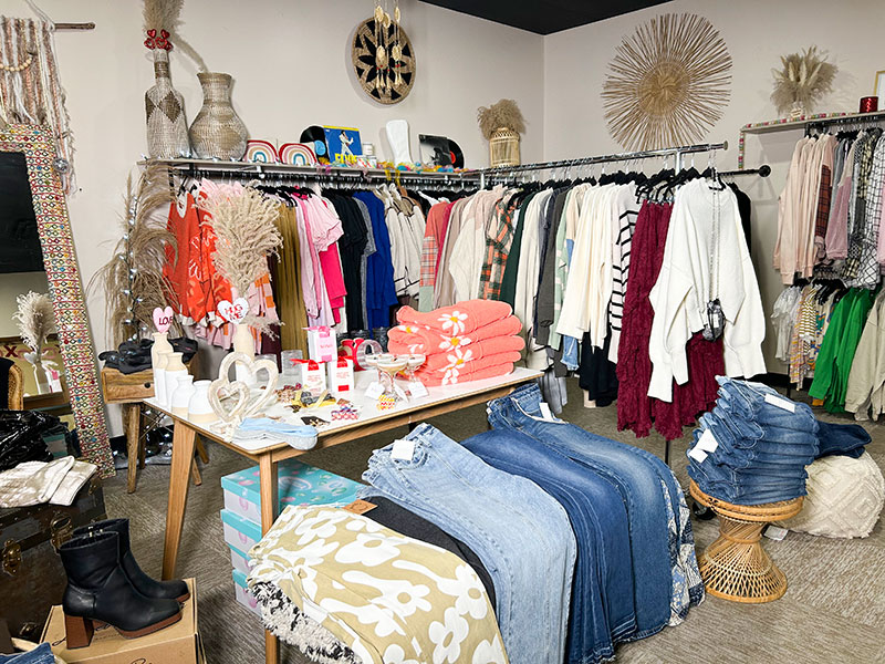 The interior of a women's clothing boutique, Hidden Harlo in Dunmore, PA, featuring racks of apparel, folded clothing and various accessories and decor items on display.