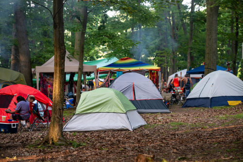 A grouping of camping tents and canopy tents in the woods as smoke from a campfire rises at Briggs Farm Blues Festival in Nescopeck, PA.
