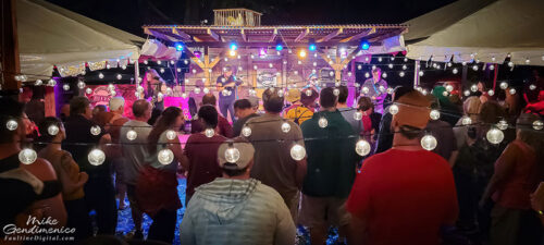 A crowd stands under strings of Edison bulbs in front of the small 