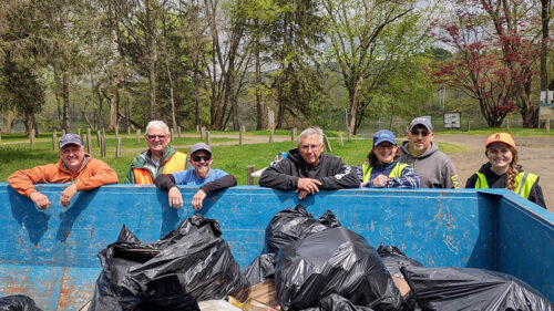 A group of men and women volunteers leaning over a dumpster full of trash they collected during their Earth Day Pick Up Paddle in Falls, PA.