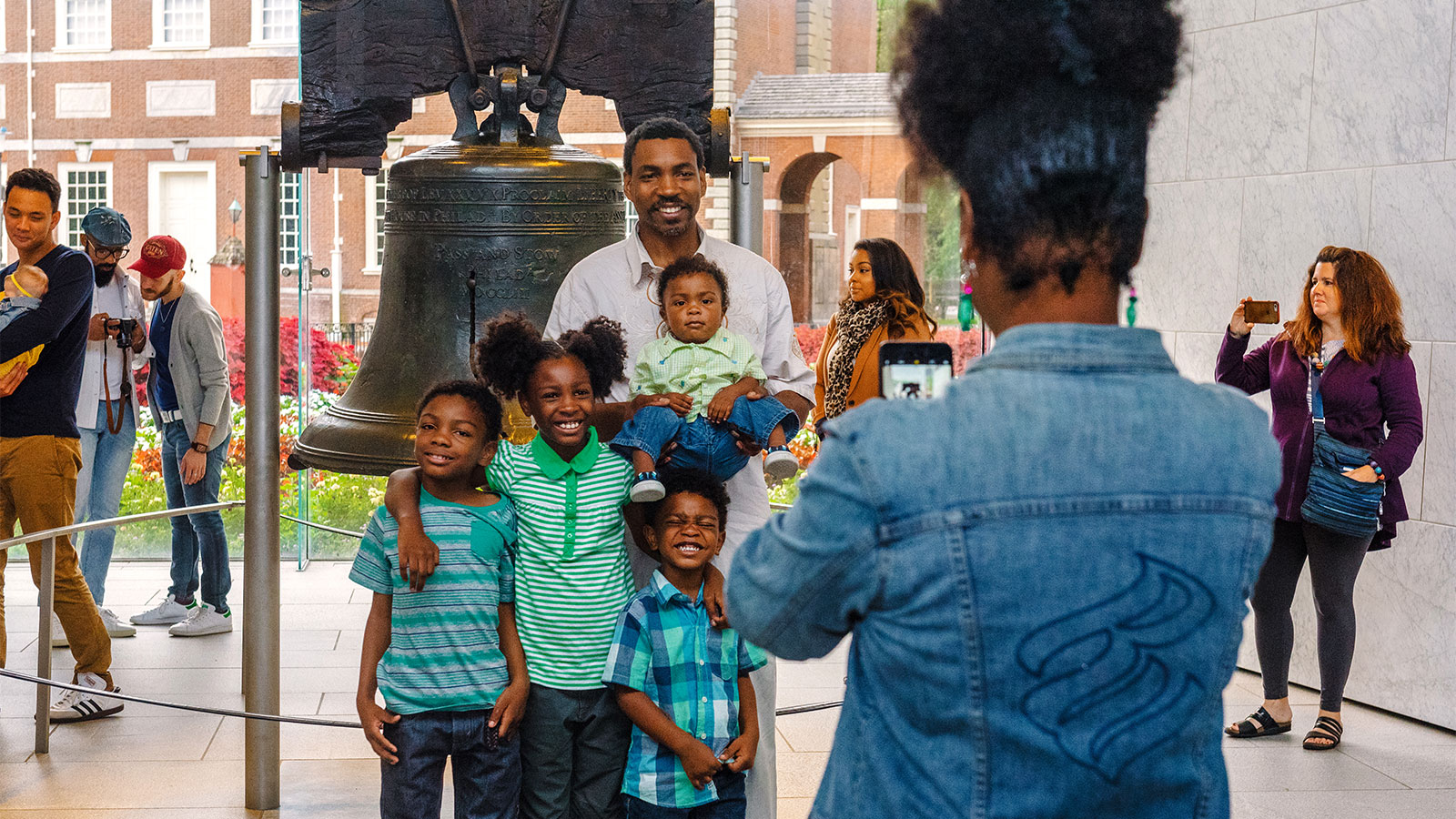 A dad and four children are posing for a photo in front of the Liberty Bell in Philadelphia Pennsylvania.