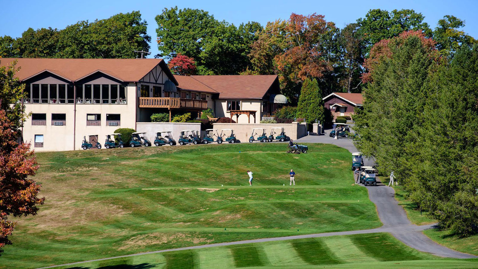 A scenic view of Hideaway Hills Golf Club in Kunkletown, PA. The golf course is lush green with neatly mowed fairways and greens. Several golf carts are parked near the clubhouse at the top of the hill.