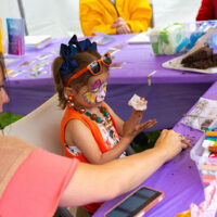 A young girl with a brightly painted face participates in making a craft at the Fine Arts Fiesta in Wilkes-Barre, PA.