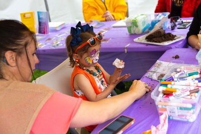 A young girl with a brightly painted face participates in making a craft at the Fine Arts Fiesta in Wilkes-Barre, PA.