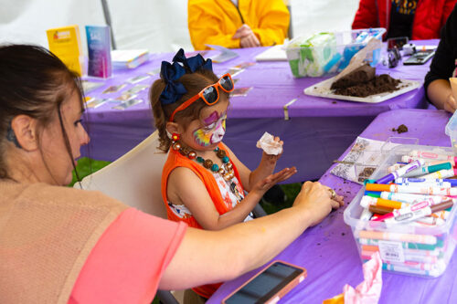 A young girl with a brightly painted face participates in making a craft at the Fine Arts Fiesta in Wilkes-Barre, PA.