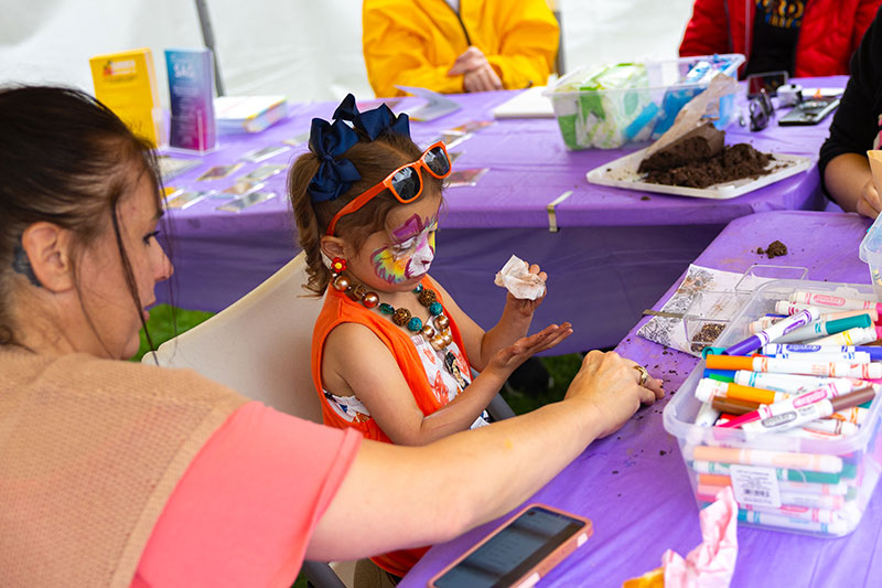 A young girl with a brightly painted face participates in making a craft at the Fine Arts Fiesta in Wilkes-Barre, PA.