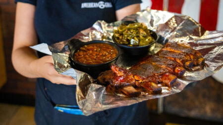 A waitress holding a large tray full of ribs, baked beans, and green beans from American Grill in Exeter, PA.