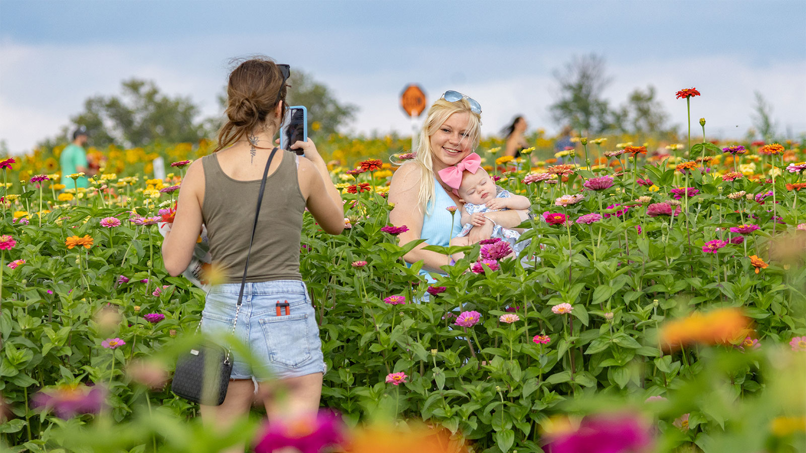 A woman poses with her baby in a zinnia field while her friend takes a photo at Lakeland Orchard & Cidery in Scott Twp., PA.