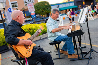 Two male musicians perform outdoors during Pittston's Second Friday Art Walk—one playing an electric guitar and the other a keyboard.